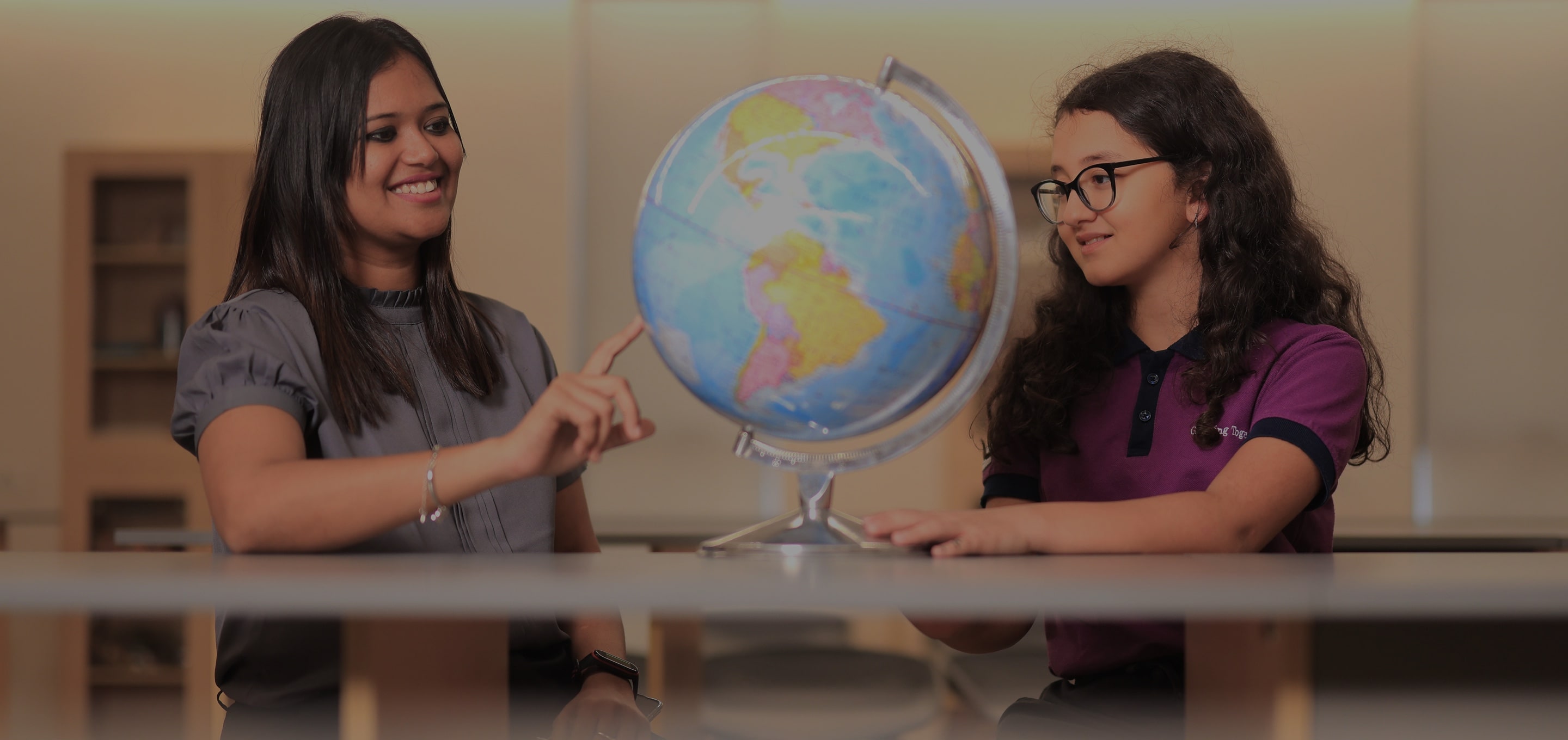 Two girls exploring world globe at Adani International School