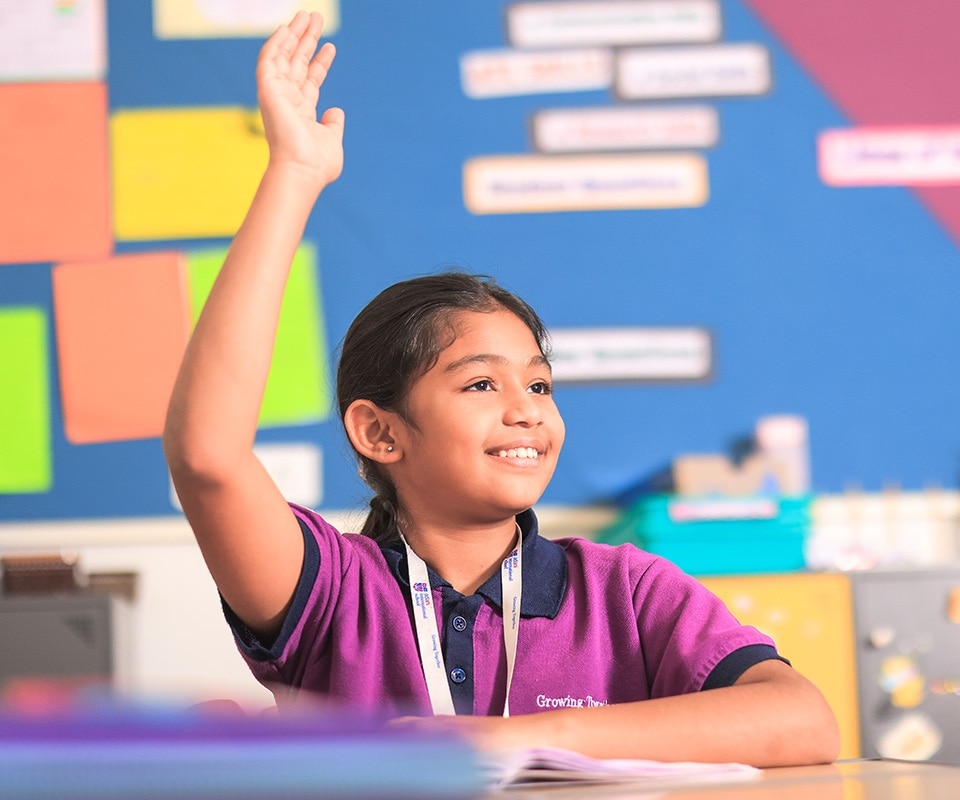 a student with raising hand in classroom at Adani International School